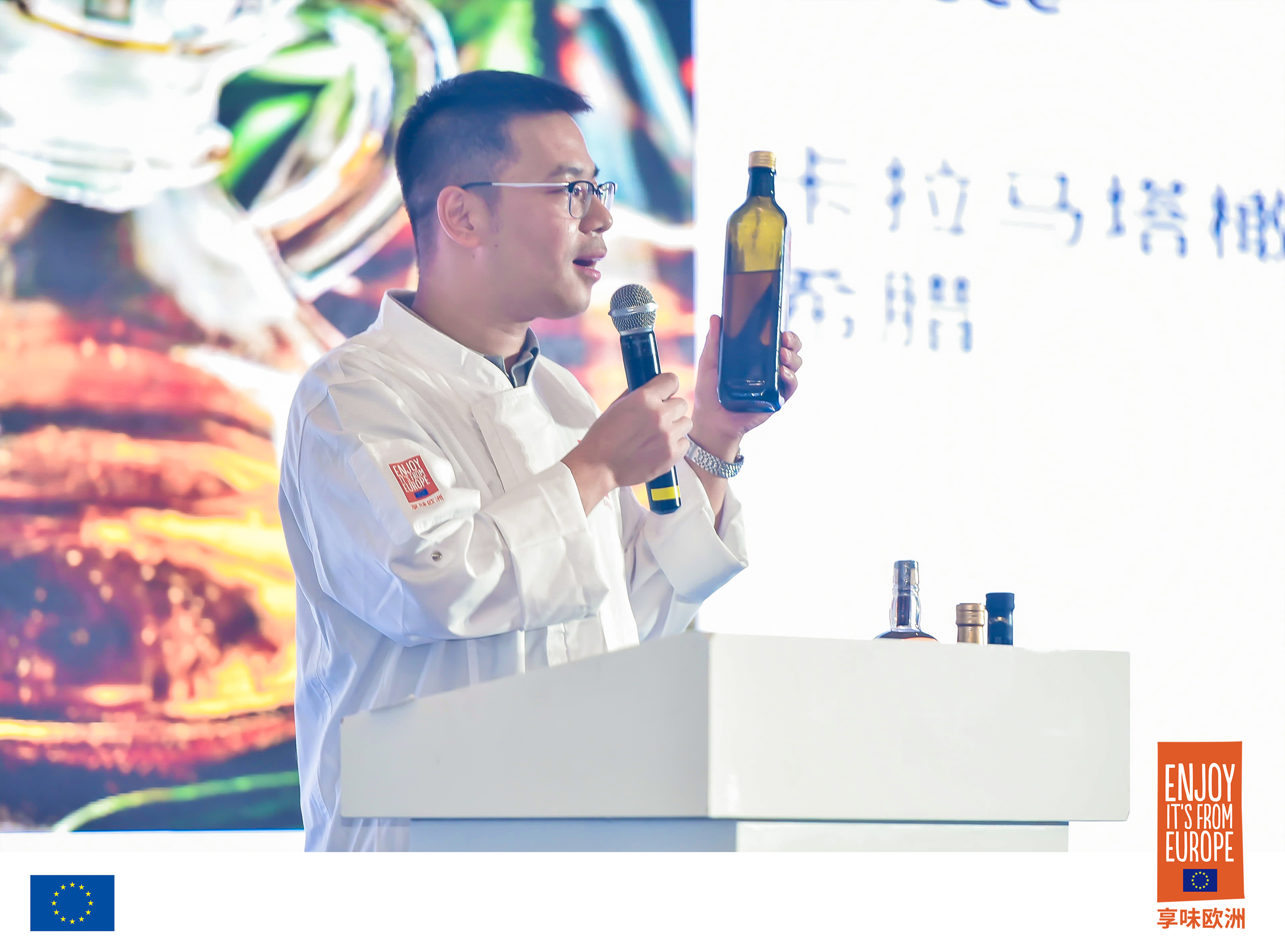 Presenter holding bottle of olive oil. 